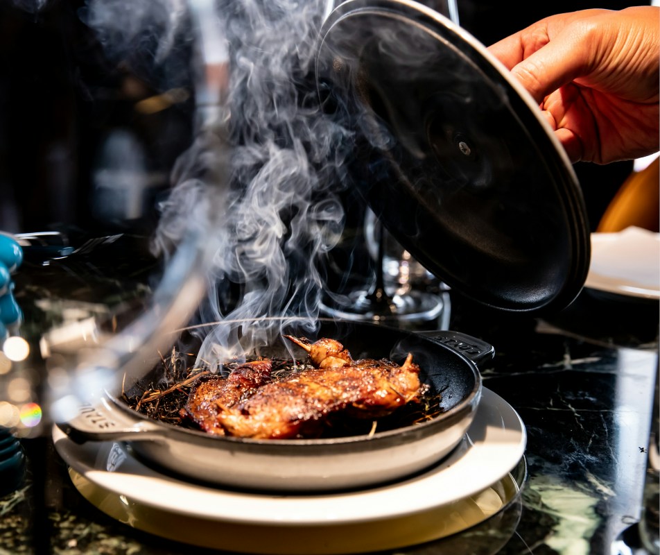 A Tuya dish presented at the table beneath a smoky glass cloche